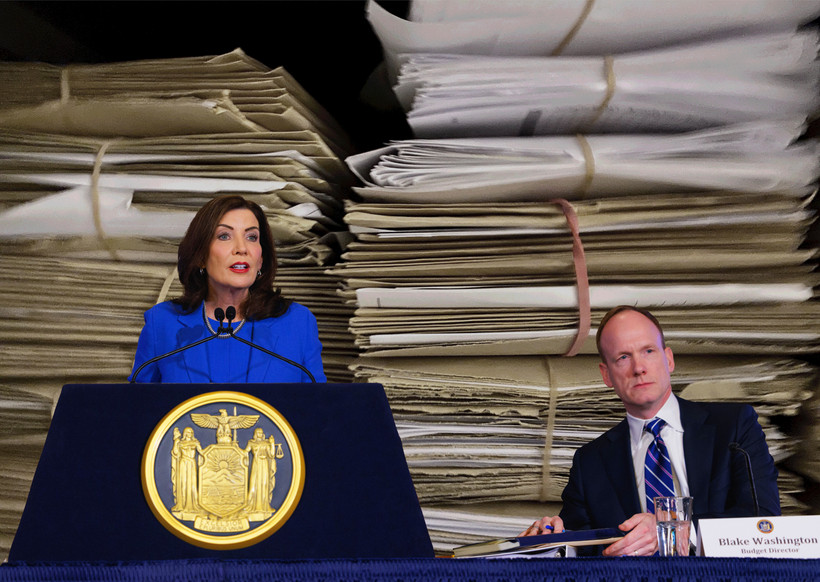 New York Governor Kathy Hochul at a podium next to her budget director, Blake Washington, with a binder, both superimposed over a photo of two stacks of paper files.