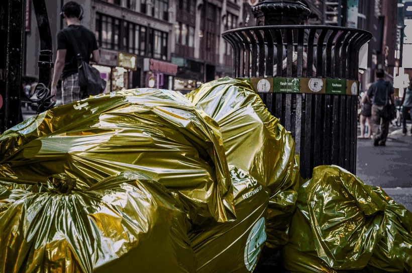 Bags of trash with a golden filter sit in front of a trash can on the curb in New York City