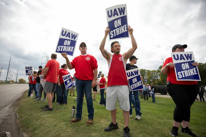 A cluster of people in red shirts hold signs saying "UAW on Strike"