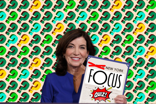 New York Governor Kathy Hochul, seated, holds a document that has been edited to read "New York Focus Quiz!" in front of a background covered in question marks.
