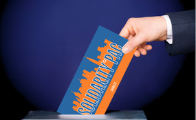A hand places a ballot with the Solidarity PAC logo in a ballot box.