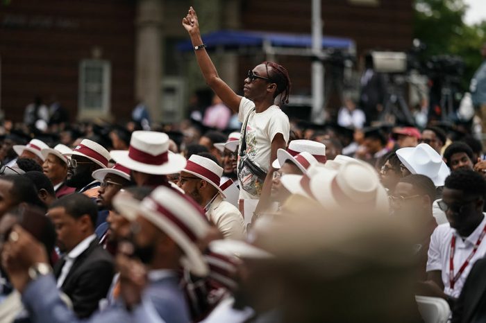 People sit in red-ribboned hats, a student stands up and snaps fingers