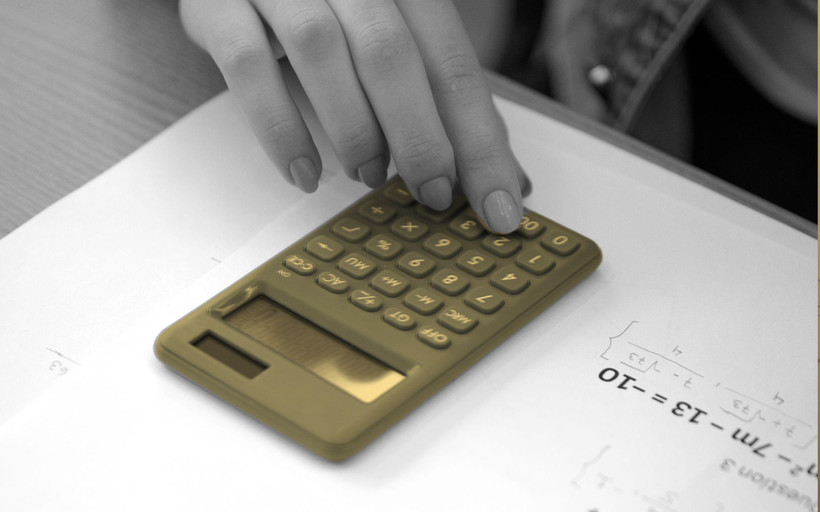 A student's hand using a calculator on a math worksheet.