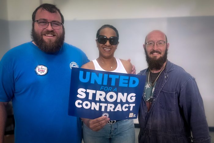 Three workers smile and hold a sign that says "United for a Strong Contract"