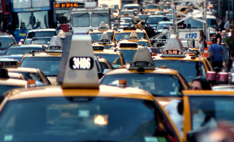 The image depicts a traffic jam in New York City, with a cluster of yellow taxi cabs at the front.