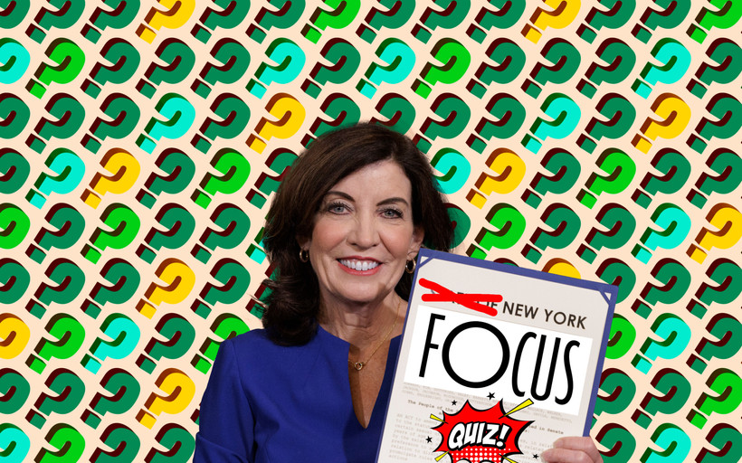 New York Governor Kathy Hochul, seated, holds a document that has been edited to read "New York Focus Quiz!" in front of a background covered in question marks.