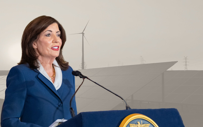 Photo montage showing NY Governor Kathy Hochul speaking on April 28 against a greyed-out backdrop of solar panels and a wind turbine.