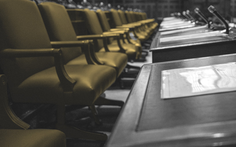 Image of a legislative chamber with many empty chairs.