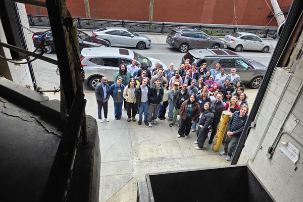 A group of about 50 people pose for a photo taken from inside a garage housing a trash compactor.