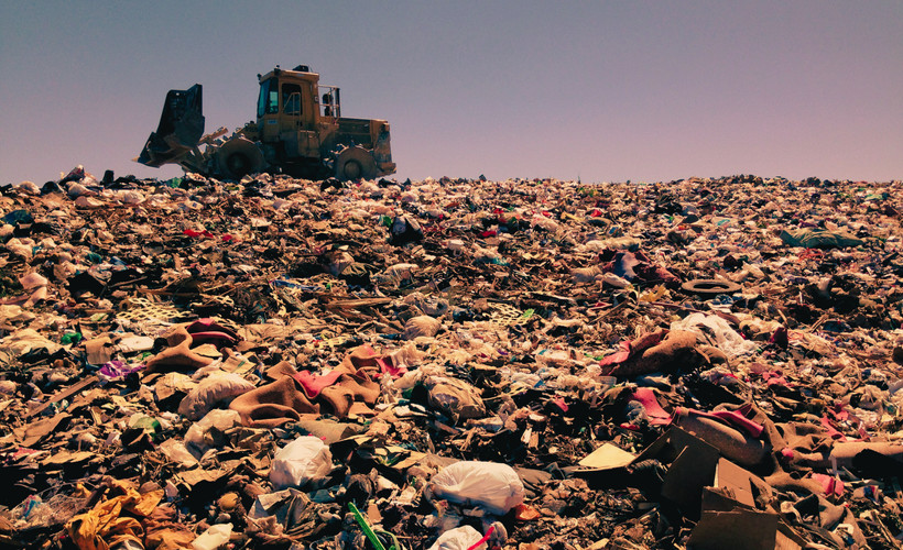 A bulldozer sits on top of a landfill full of trash.
