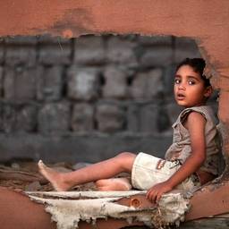 A child sits sideways looking through a torn canvas wall.