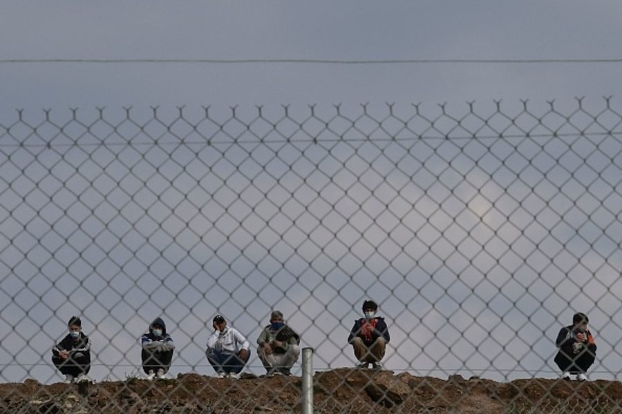 Six people crouching behind a wire fence