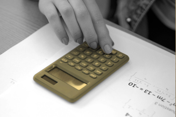 A student's hand using a calculator on a math worksheet.