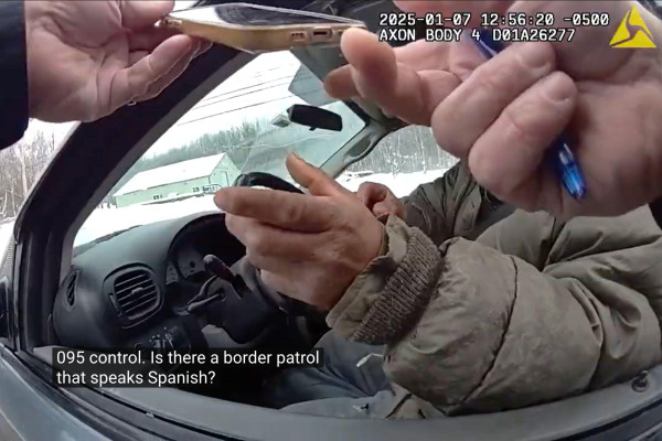 A screenshot from a police body camera shows a person in a car, his face obscured by the officer's hands holding a phone. The caption shows the officer saying "Is there a border patrol that speaks Spanish?"