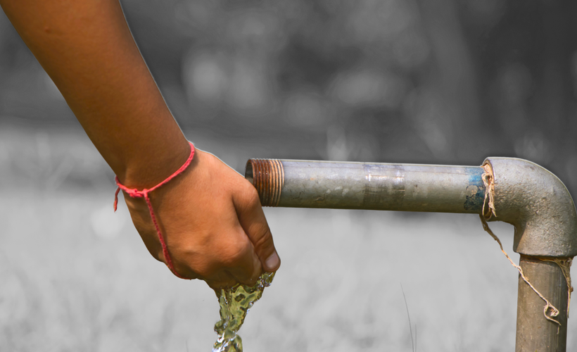 Someone rinses their hand with water from a rusty lead pipe in a park.