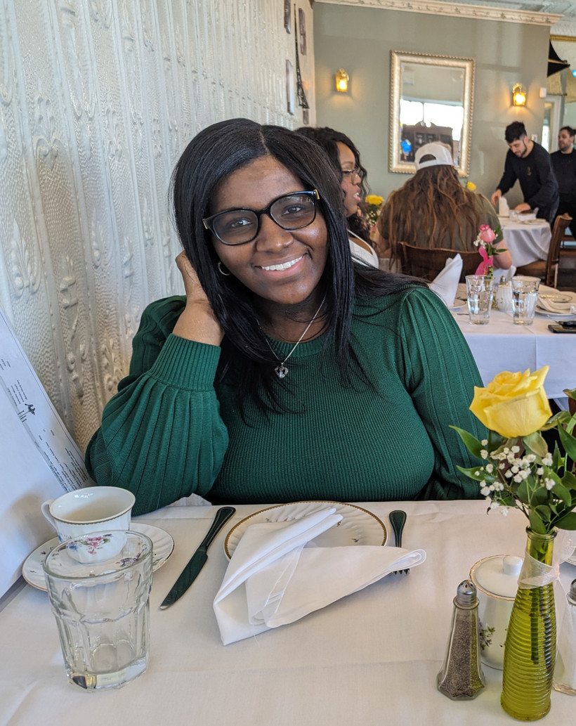Sophie-Anais Renois sits smiling at a restaurant, a yellow rose in a vase on the table in front of her.