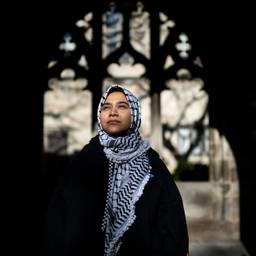 A woman wearing a keffiyeh as a hijab looks ahead.