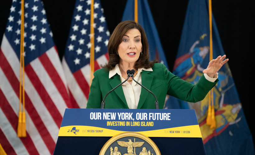 New York State Governor Kathy Hochul stands in front of American flags and behind a podium reading "Our New York, Our Future."