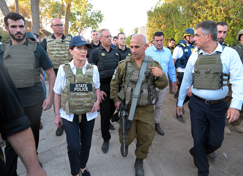 Governor Kathy Hochul, in a bulletproof vest reading "STATE POLICE," walks with Israeli hosts in Kfar Aza.