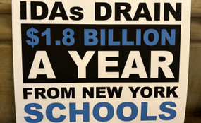 A sign reads "IDAs DRAIN $1.8 BILLION A YEAR FROM NEW YORK SCHOOLS."