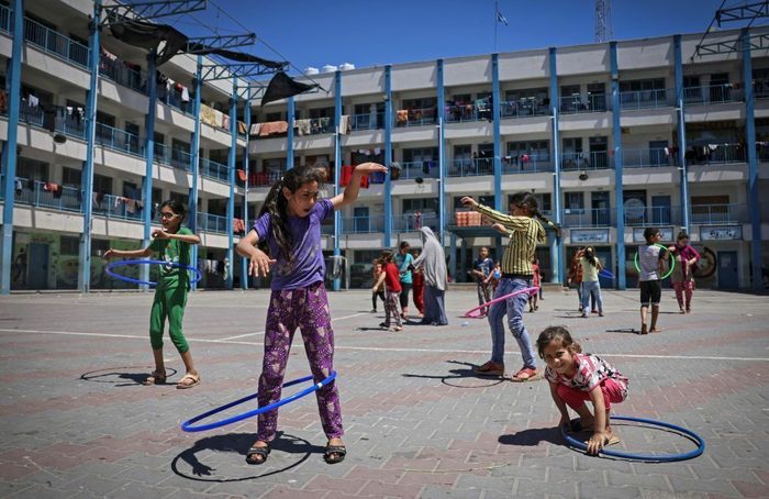 A handful of Gaza girls play with hula hoops. In the background is a school building where laundry is hanging.