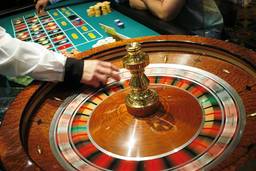 Closeup of a hand spinning a roulette wheel, with hands moving betting tokens in the background.