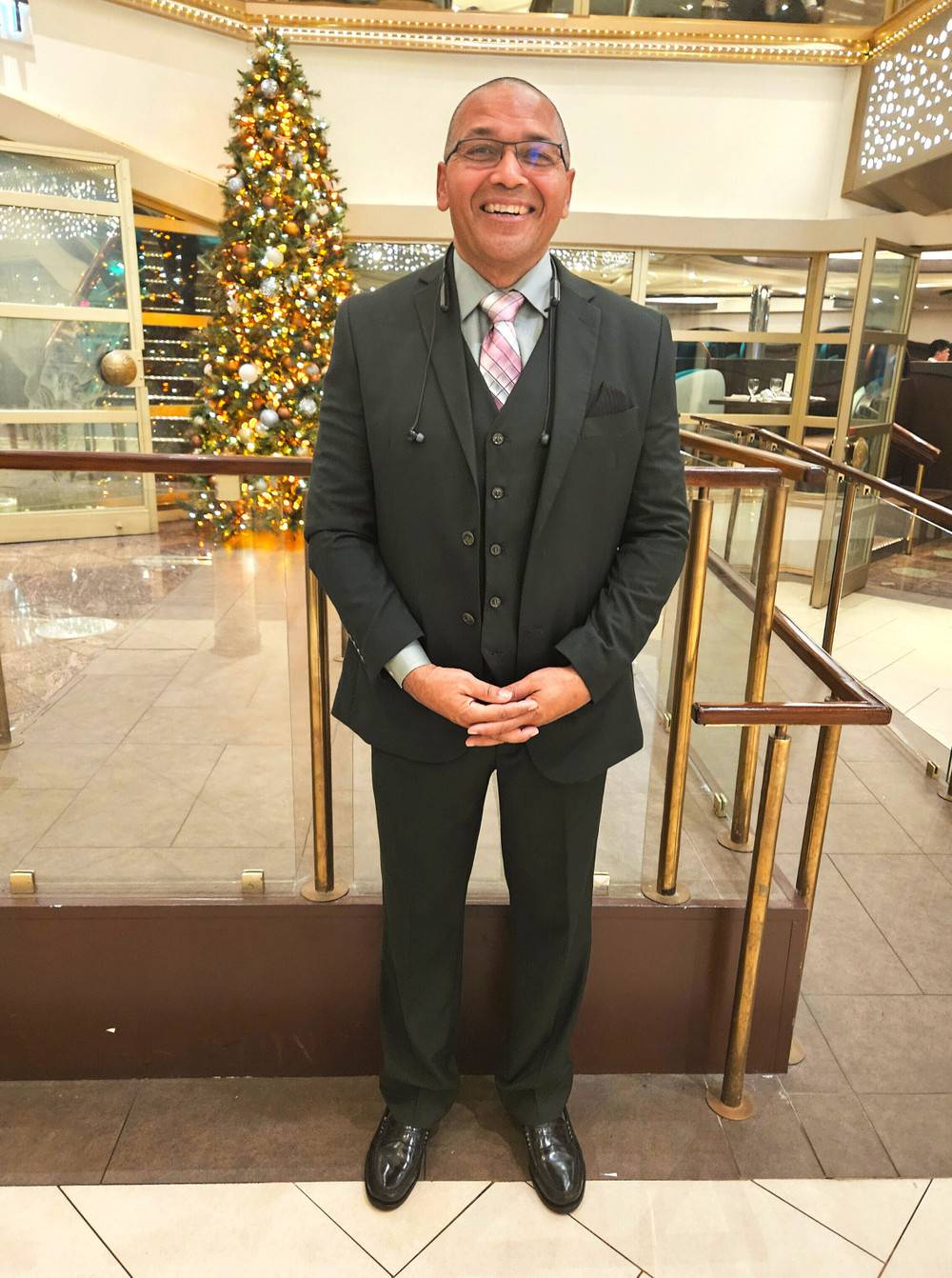 A man in a suit stands smiling in front of a gold interior space with a Christmas tree in the background.