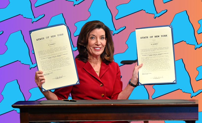 Governor Kathy Hochul holds two signed bills, superimposed over a background showing the state of New York.