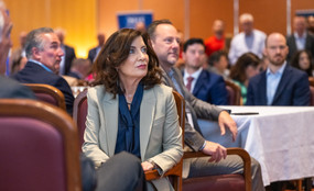 Governor Kathy Hochul sits in a chair at a breakfast meeting and looks up.