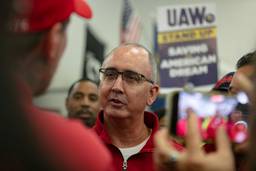 Closeup of Shawn Fain mid-speaking to a worker who is facing away from the camera; UAW strike sign in the background.
