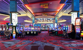 Photo of a casino floor with rows of brightly lit video lottery terminals and a single player sitting to the left in front of a terminal.