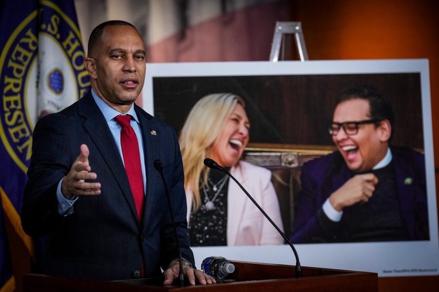 U.S. House Minority Leader Hakeem Jeffries (D-N.Y.) speaks in front of a poster-sized image of Reps. George Santos and Marjorie Taylor Greene cackling.