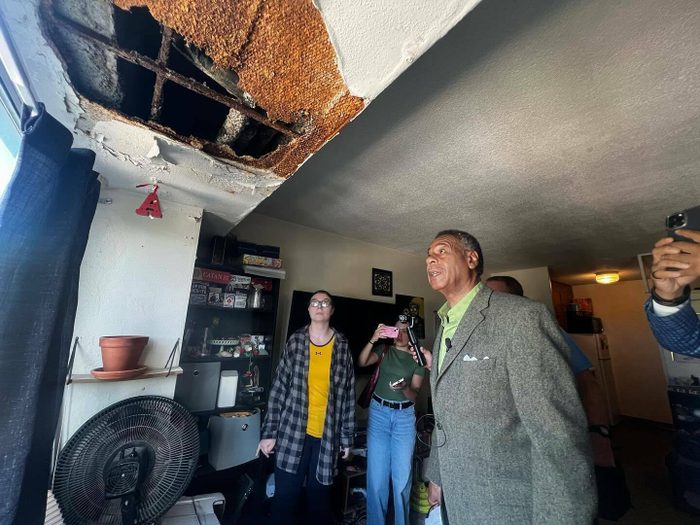 Three people stand looking up at a large hole in a ceiling.