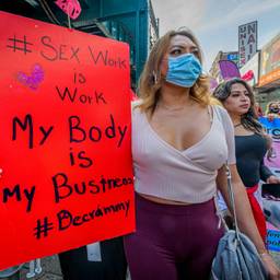 "Sex work is work / My body is my business / #Decrim" reads a large red sign held by a marcher