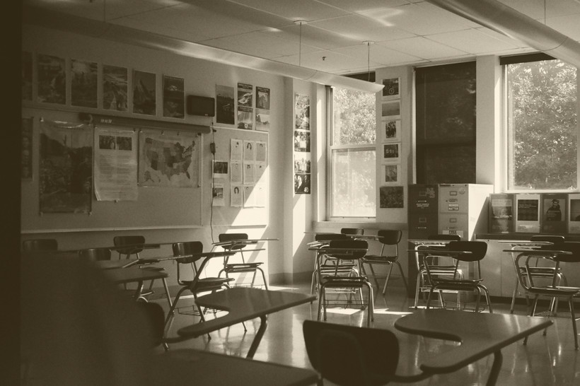 An image of a classroom with two windows and many empty desks.