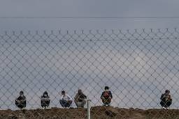 Six people crouching behind a wire fence