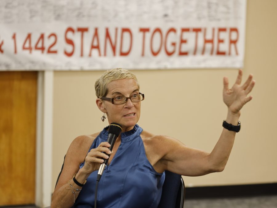 Jane McAlevey addresses a crowd before a banner that reads in part "STAND TOGETHER."