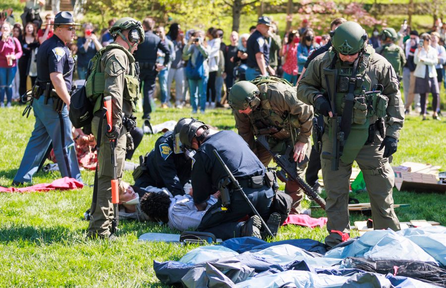 Two state police troopers hold down two protestors on the grass at Indiana University while several other swat team members look on.