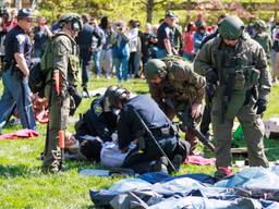 Two state police troopers hold down two protestors on the grass at Indiana University while several other swat team members look on.