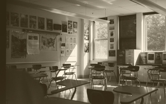 An image of a classroom with two windows and many empty desks.