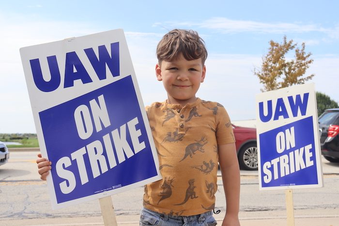 Closeup of a child in a tan shirt holding a "UAW on Strike" sign