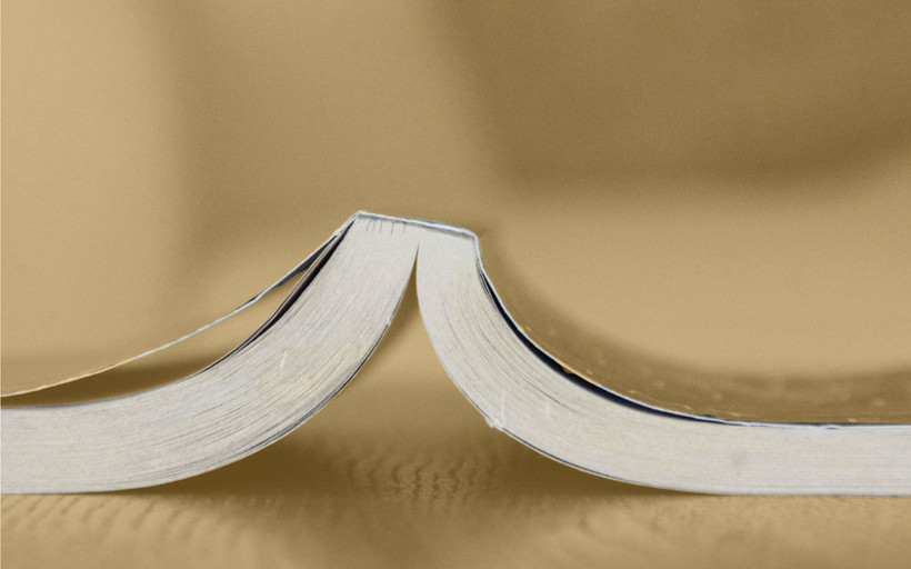 A book lies open and face-down on a desk.
