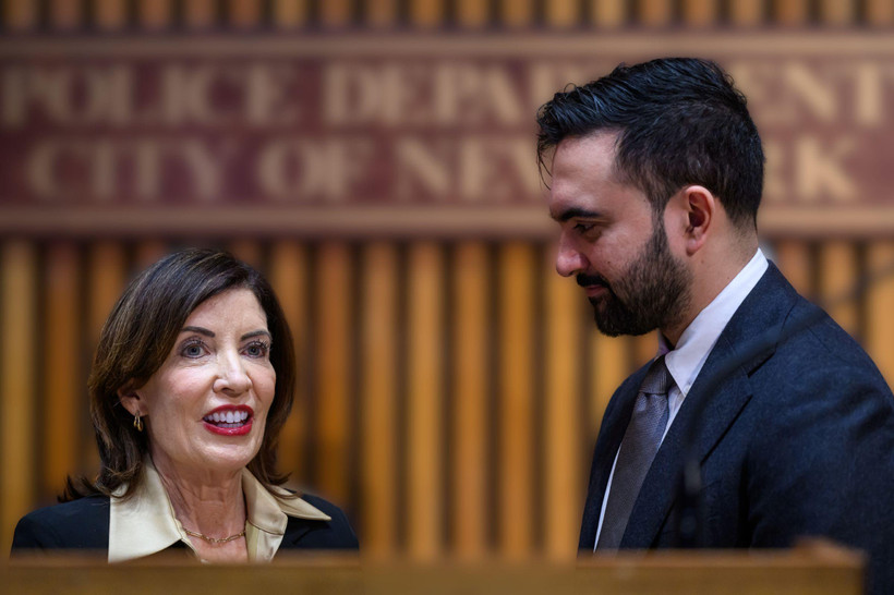 NYC Mayor Zohran Mamdani, in profile, looks at Governor Kathy Hochul, who looks outwards. The two stand close to each other behind a podium.