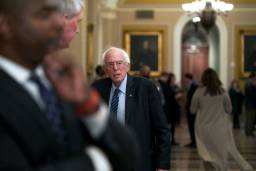 An image of Bernie Sanders in a suit and tie, briefly pausing on his walk to Senate chambers.