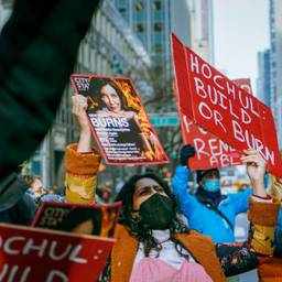 In a protest crowd, a closeup on one protester holding a sign that says "Hochul: Build of Burn"