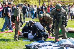 Two state police troopers hold down two protestors on the grass at Indiana University while several other swat team members look on.