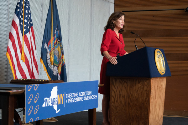 New York Governor Kathy Hochul stands at a podium next to a sign reading "treating addiction and preventing overdoses."