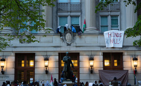 Student protesters gather at Columbia's Hamilton Hall or "Hind's Hall," renamed after Hind Rajab, a six-year-old Palestinian girl who was shot to death with paramedics on an IDF-supplied emergency route. On the right, they hang a banner that says "HIND'S HALL." Protesters sit up high on a facade.