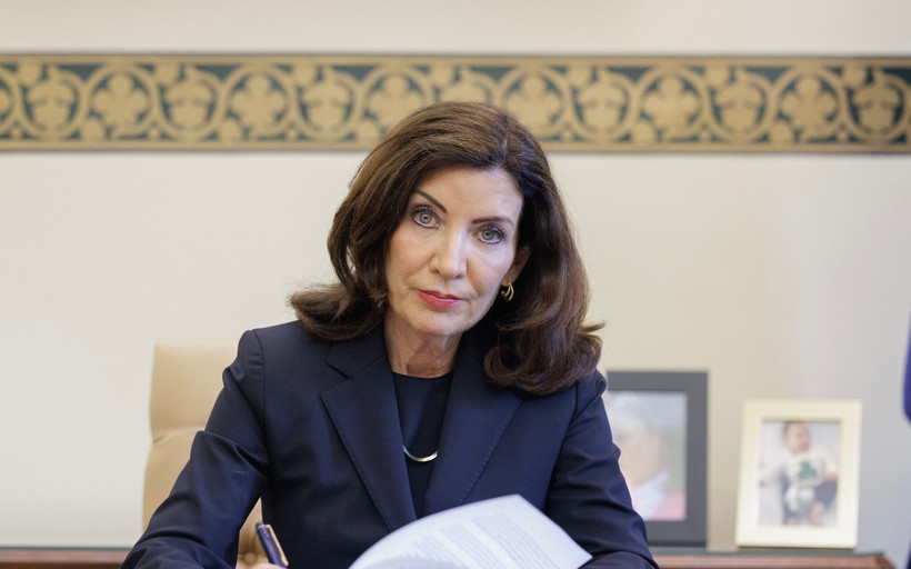 Kathy Hochul stares into the camera while signing papers