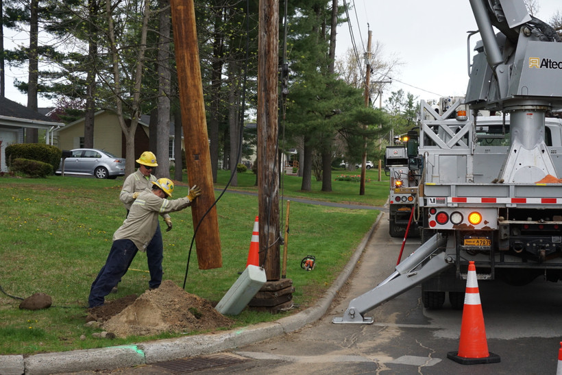 Crew lifts a utility pole from a hole in the ground in Massena, New York.